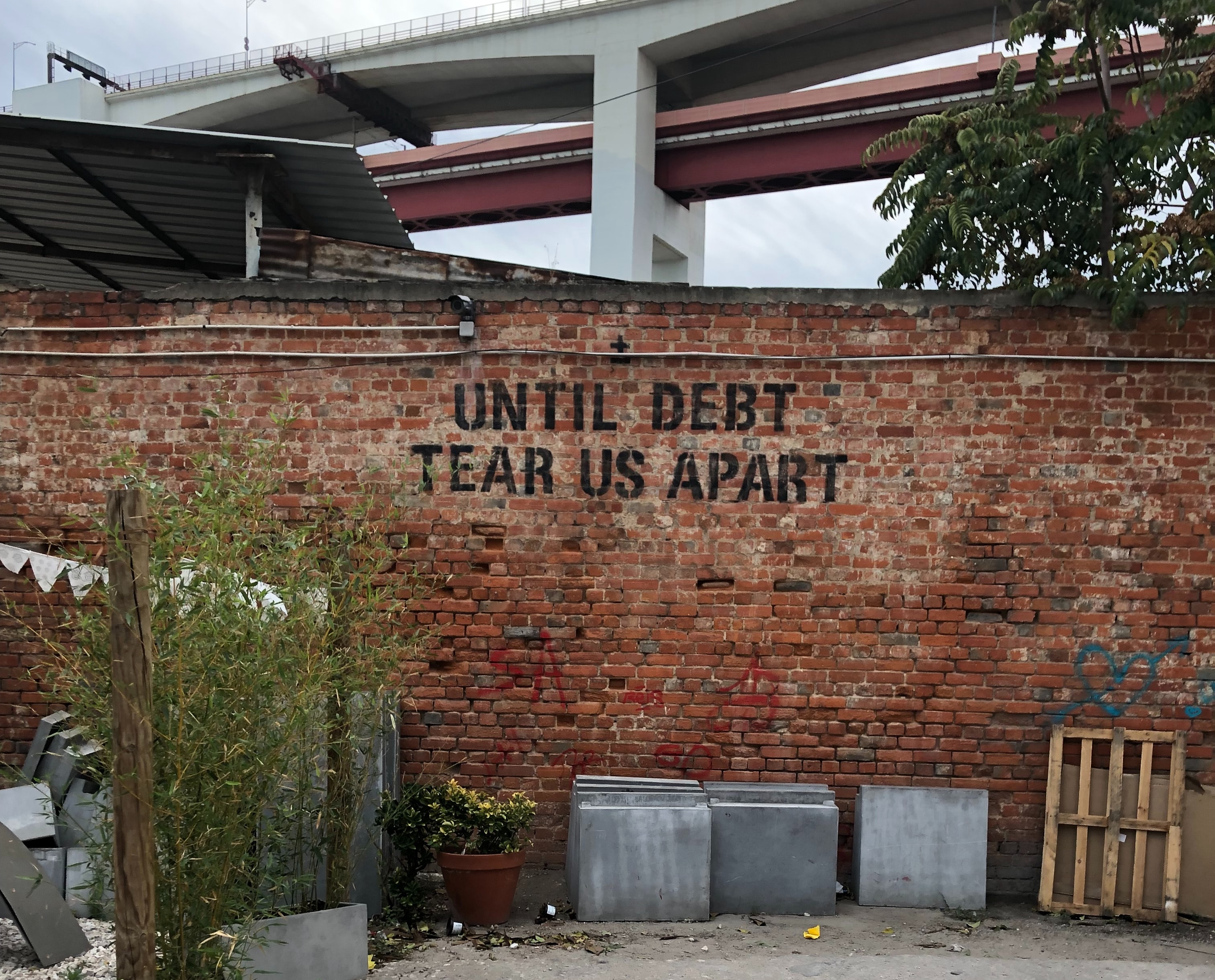 Black spray paint graffiti on brick wall that reads Til Debt Tear Us Apart