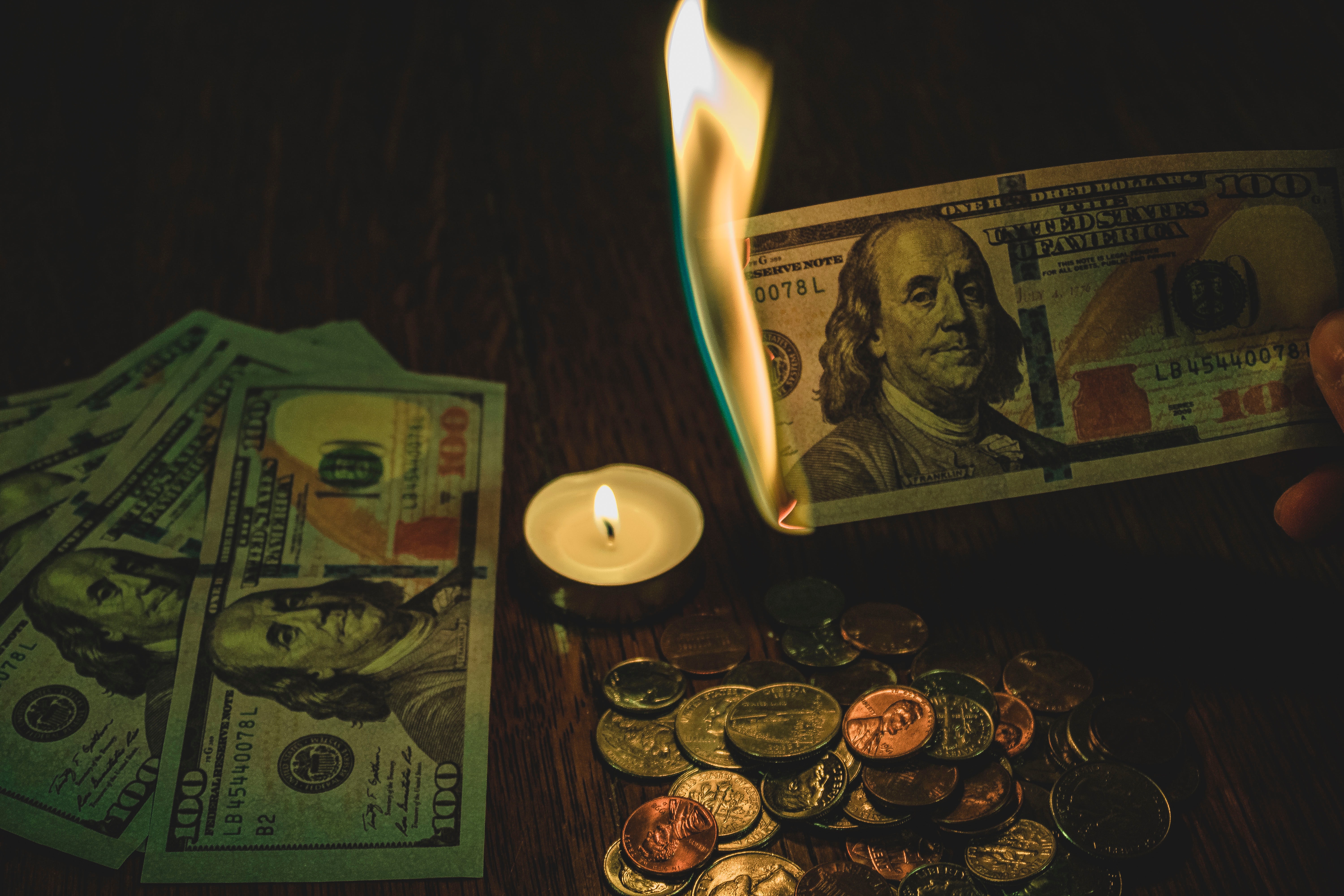 several $100 bills, one being burned over a candle